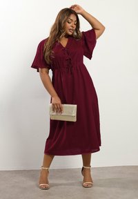Burgundy midi-mekko, jossa on lyhyet hihat, kootut vyötärö ja kaarroke yksityiskohdat. Yhdistetty metallinhohtoiseen kultalaukkuun ja vaaleanbeigeihin korkokenkiin.
