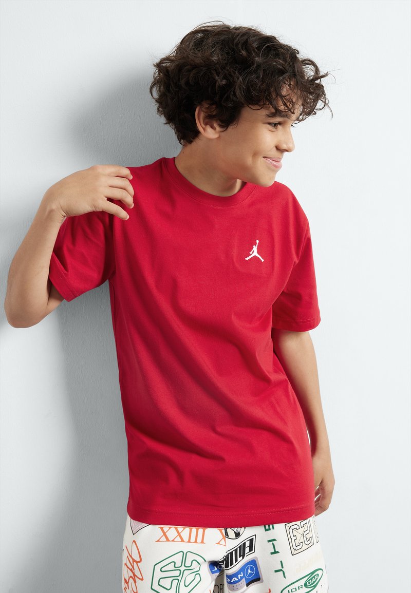 T-shirt en coton rouge avec un col rond et des manches courtes, arborant un logo Jordan blanc sur la poitrine gauche.