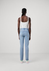 Jeans in denim azzurro chiaro a gamba dritta con tasche posteriori e una leggera strappatura. Abbinati a un top a canotta bianco a coste e sneakers colorate.