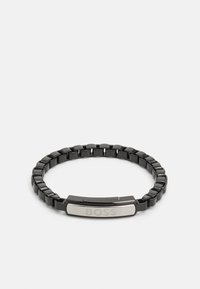 Pulsera de metal negro con una banda flexible, una placa central de plata con la palabra "BOSS" grabada y una superficie pulida.