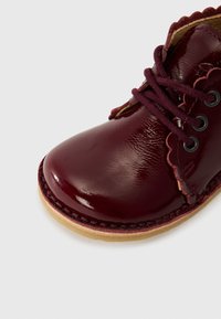 Chaussure en cuir bordeaux avec une finition brillante, bords festonnés, lacets ronds et semelle en cuir brun cousue. Design à bout rond.