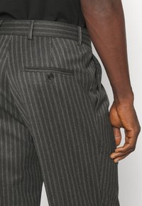 Szare spodnie w szare prążki o prostym kroju, z tylną kieszenią zapinaną na guzik oraz teksturowaną tkaniną.