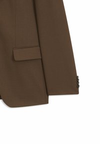 Manche et poche de veste marron avec quatre boutons foncés au poignet sur fond blanc.