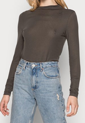 Woman wearing a fitted dark brown long-sleeve top tucked into high-waisted light blue distressed jeans.