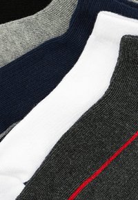 Calcetines surtidos con una mezcla de colores: negro, gris, azul marino, blanco y gris oscuro, con un acento rojo en un par. Tela de punto texturizada.