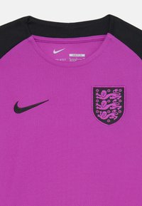 T-shirt de sport Nike violet avec des accents noirs ; présente un tissu texturé et un écusson brodé avec des lions et des détails floraux. Design ajusté.