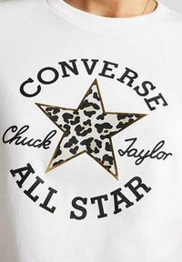 Camiseta blanca con una gran estrella de estampado de leopardo negro y beige, con "CONVERSE" y "ALL STAR" en letras negras en negrita.