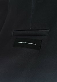 Primer plano de una tela negra con un bolsillo cosido y una etiqueta negra que dice "MWM" x movimiento de ola moderna en texto blanco.