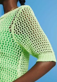 Hellgrüner, gestrickter Pullover mit einem lockeren, offenen Strickmuster. Kurze, mit Bündchen versehene Ärmel und strukturierter gerippter Saum. Der Hintergrund ist blau.