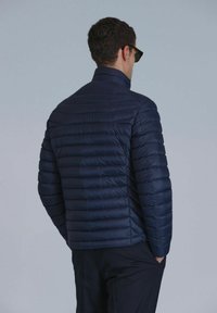 Navy puffer jacket with horizontal stripes, high collar, and lightweight material. Smooth texture, fitted design, and no visible hardware.