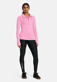 Rosa långärmad topp med en kvartslång dragkedja och logotyp, matchad med svarta leggings med en logotyp på ett ben, båda anpassade för sportkläder.