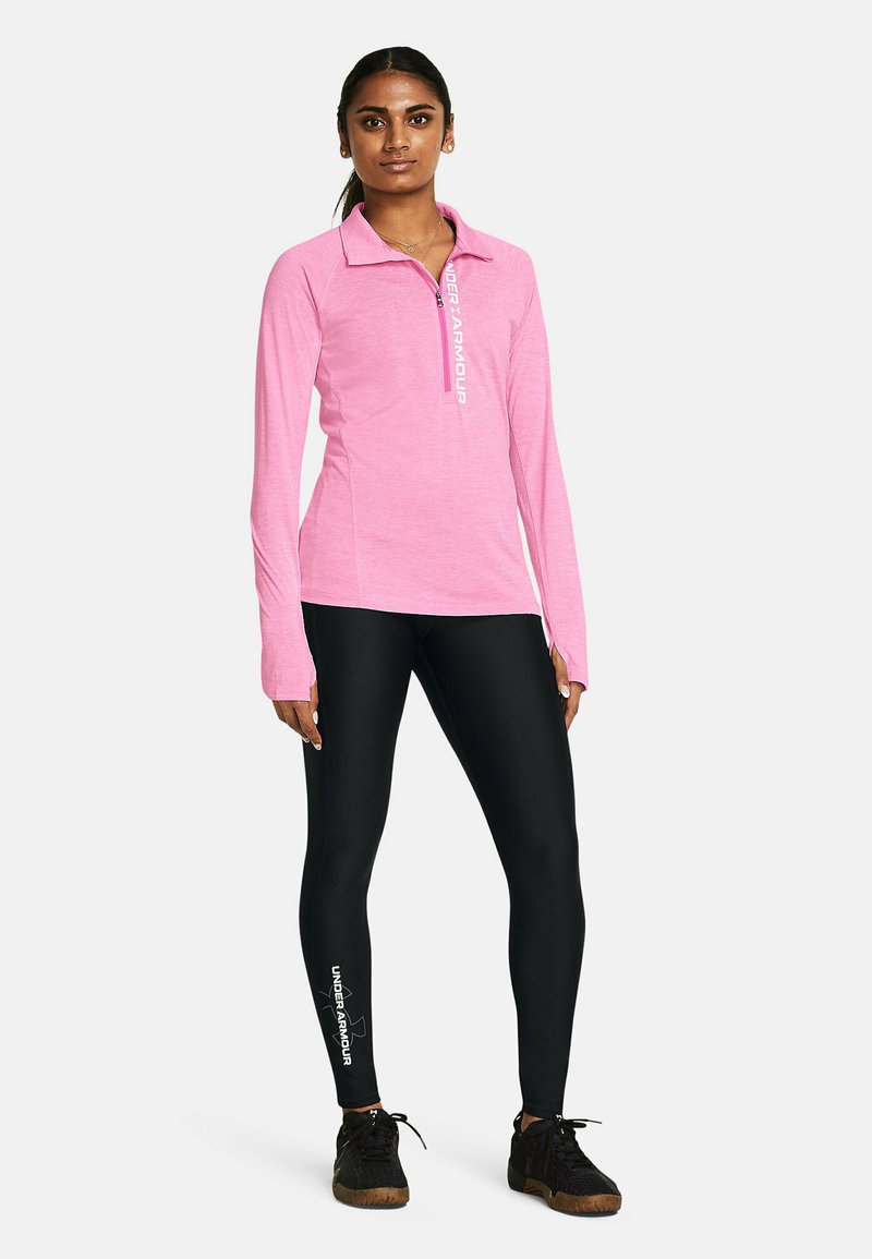 Roze langemouwen bovenstuk met een ritssluiting van een kwart lengte en een logo, gecombineerd met zwarte leggings met een logo op één been, beide geschikt voor sportkleding.