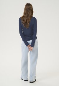 Navy long-sleeve top paired with light blue wide-leg jeans. The top features a fitted design, and the jeans have a classic denim texture.