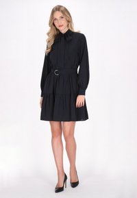 Robes noires avec un col haut à nœud, des manches longues et une jupe à volants. Comprend une ceinture en tissu avec une boucle circulaire. Texture lisse.