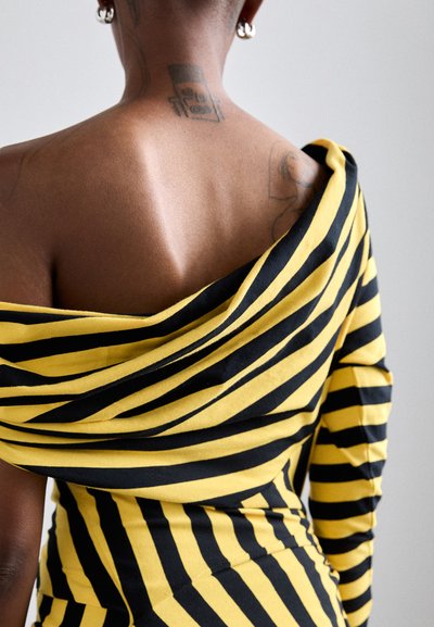 Off-shoulder klänning i svart och gula ränder, med draperad halsringning, figurnära silhuett och slät tygtextur.