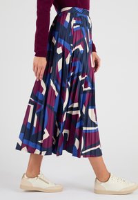 Gonna maxi plissettata con un audace motivo astratto in blu navy, bordeaux, bianco e blu. Indossata con sneakers di colore chiaro.