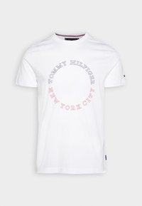 Camiseta blanca de algodón con un estampado circular que incluye el texto "TOMMY HILFIGER" y "NEW YORK CITY" en gris y rojo. Mangas cortas, escote redondo.