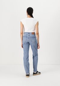 Jeans de ganga azul de cintura alta com um corte descontraído, apresentando bolsos traseiros e um emblema de couro castanho na cintura.