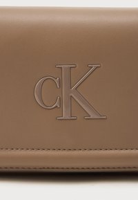 Læraktig lommebok i tan-farge med preget "CK"-logo, glatt tekstur og synlig søm langs kantene.