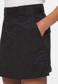 Svart kort kjol med en strukturerad midja, sidofickor och en slät yta. Har en enkel design och en lätt utsvängd form.