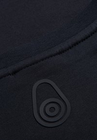 Mörkblå bomullstyg med en strukturerad yta, med en svart gummilogotyp centralt placerad, som framhäver cirkulära designelement.