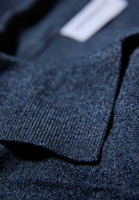 Dunkelblaues gestricktes Poloshirt mit rippenstrukturierter Kragen, ausgestattet mit einem glatten Stoff und subtilen Melange-Muster. Etikett in der Nähe des Kragens sichtbar.