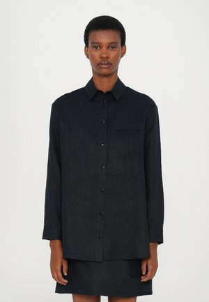 Svart langermet skjorte med knappefront, krage og en enkelt brystlomme med broderte detaljer. Laget av teksturert stoff.