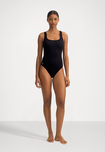 Melnā viengabala peldkostīmā ar kvadrātveida izgriezumu, platām siksnām un pieguļošu nogriezumu. Gluda tekstūra ar minimālu zīmolu uz gurniem.