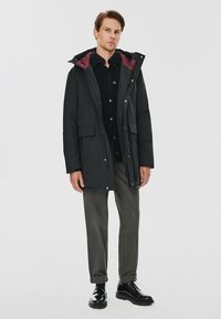 Czarna parka z bordowym podszyciem, z kapturem, dwoma przednimi kieszeniami z klapką i zapięciem na napy, zestawiona z ciemnymi spodniami i czarnymi butami.