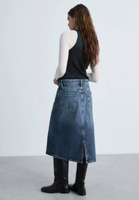 Denim rok met een rechte snit, van licht naar donkerblauw verloop, achterzakken en een split middenachter, gecombineerd met kniehoge bruine laarzen.