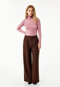 Różowa bluzka z długim rękawem i golfem w połączeniu z brązowymi, szerokimi spodniami z wysokim stanem. Gładki materiał, dopasowany krój i subtelne zakładki.