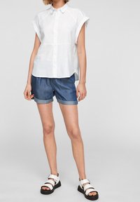 Camicia bianca a maniche corte con colletto, abbinata a pantaloni shorts di denim. I pantaloni shorts sono arrotolati all'orlo. Indossata con sandali bianchi e neri.