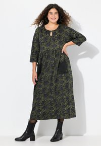 Černé šaty s zeleným růžovým vzorem, tříčtvrteční rukávy, výstřih ve tvaru klíče, nařasený pas a dvě černé kapsy. Doplňují se s černými kotníkovými botami.