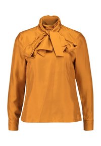 Pitkähihainen pusero sinapinkeltaista satiinia. Ominaisuuksina korkea kaulus, jossa on solmittava yksityiskohta edessä, sekä sileä ja kiiltävä pinta.