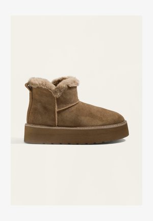 Rjav semiš gležnjarji s krznom na ovratniku, ravnim gumijastim podplatom in trakom za vlečenje na zadnji strani. Gladka tekstura z detajlom šivanja.