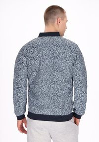 Bomber jacket blu navy con un intricata fantasia astratta bianca, polsini e orlo a costine e un colletto classico. Tessuto leggero.