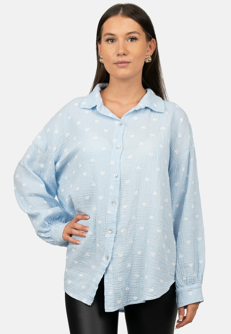 Lichtblauw overhemd van een gestructureerde katoenstof, met een overal wit hartpatroon, kraag en lange, iets opgeblazen mouwen.