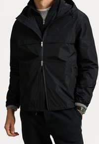 Musta vetoketjullinen huppari, jossa sileä pinta, pystypaita ja harmaat kontrastihihansuut. Edessä hopeanväriset vetoketjuyksityiskohdat.