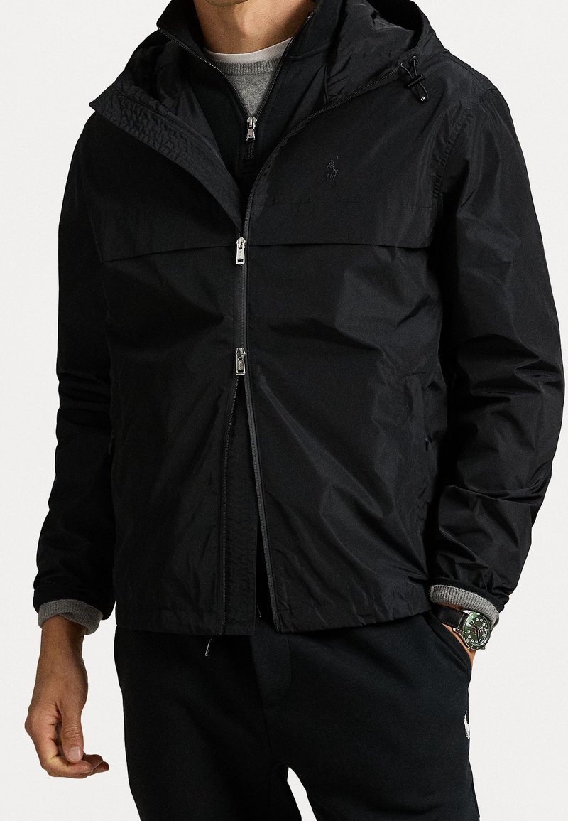 Musta vetoketjullinen huppari, jossa sileä pinta, pystypaita ja harmaat kontrastihihansuut. Edessä hopeanväriset vetoketjuyksityiskohdat.