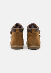 Braune Wildleder-Stiefeletten mit einem dunkelbraunen Lederkragen und Klettverschlüssen. Die Sohlen weisen eine feine Nahtdetails auf.