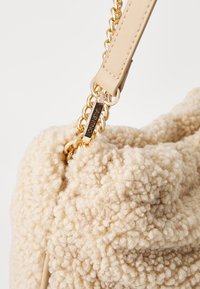 Beige strukturerad väska med en mjuk, fluffig yta, med en guldkedja och läderrem fäst med ett metallspänne.