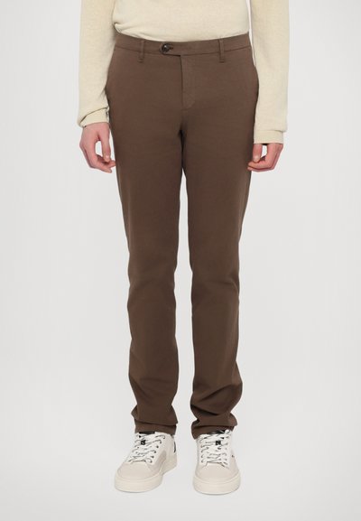 Brune bomuldsbukser med slim fit, knaplukning og sidelommer, parret med hvide sneakers med sorte accenter.