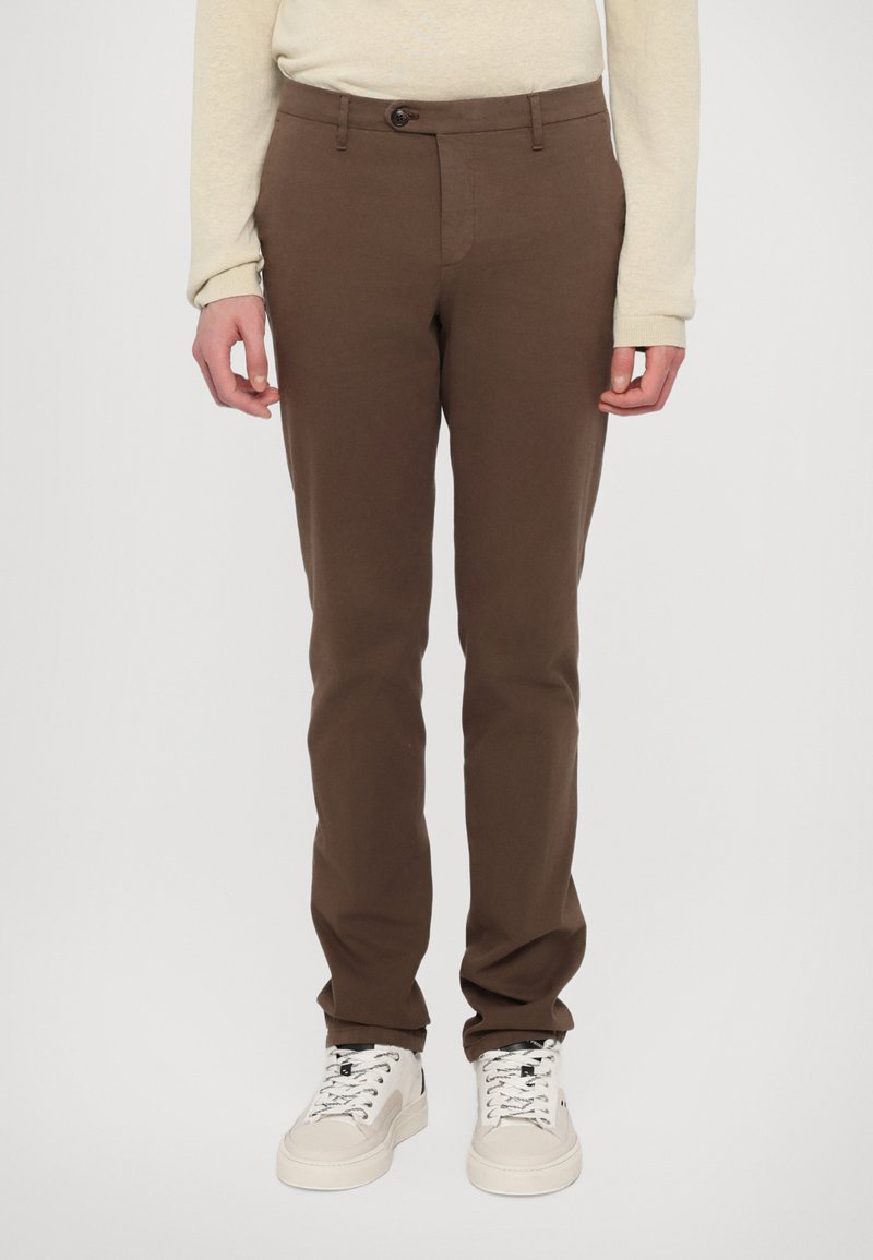 Pantaloni din bumbac maro, cu croi slim, închidere cu nasture și buzunare laterale, asortați cu adidași albi cu accente negre.