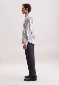 Camicia a maniche lunghe a scacchi in bianco e blu navale, con colletto button-down, vestibilità rilassata, abbinata a pantaloni neri slim-fit e scarpe nere.
