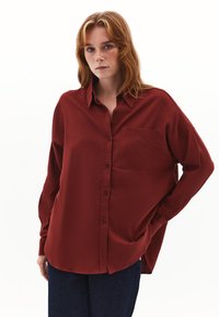 Camicetta rossa con bottone, dotata di taschino sul petto, vestibilità rilassata e maniche lunghe, realizzata in un tessuto morbido e leggero.