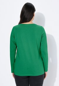 Zielony top z długim rękawem i okrągłym dekoltem, wykonany z miękkiego materiału. Charakteryzuje się prostym krojem, minimalistycznym designem i niewielką rozciągliwością.