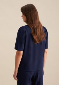 Blusa blu navy con maniche a sbuffo e design semplice. Tessuto morbido con una consistenza liscia. Nessun motivo o decorazione visibile.