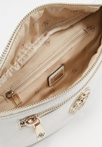 Sisätilat valkoisessa teksturoidussa nahkabagissa ovat beigeä vuoritulosta, jossa on vetoketjullinen tasku ja brändilogo-tarra. Kultaiseen sävyyn huolitellut yksityiskohdat.