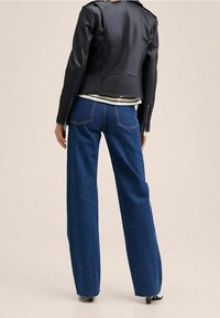 Veste en cuir noir à coupe ajustée, associée à un jean denim bleu à jambes larges. Le jean présente des poches arrière apparentes et un ourlet effiloché.