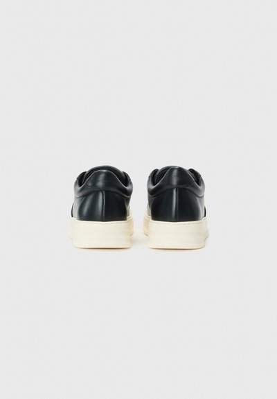 Mustat nahka sneakersit, joissa on kermaisen värinen kumipohja, tyylikkäällä pinnalla ja pyöristetyllä kantapäällä mukavuutta varten.